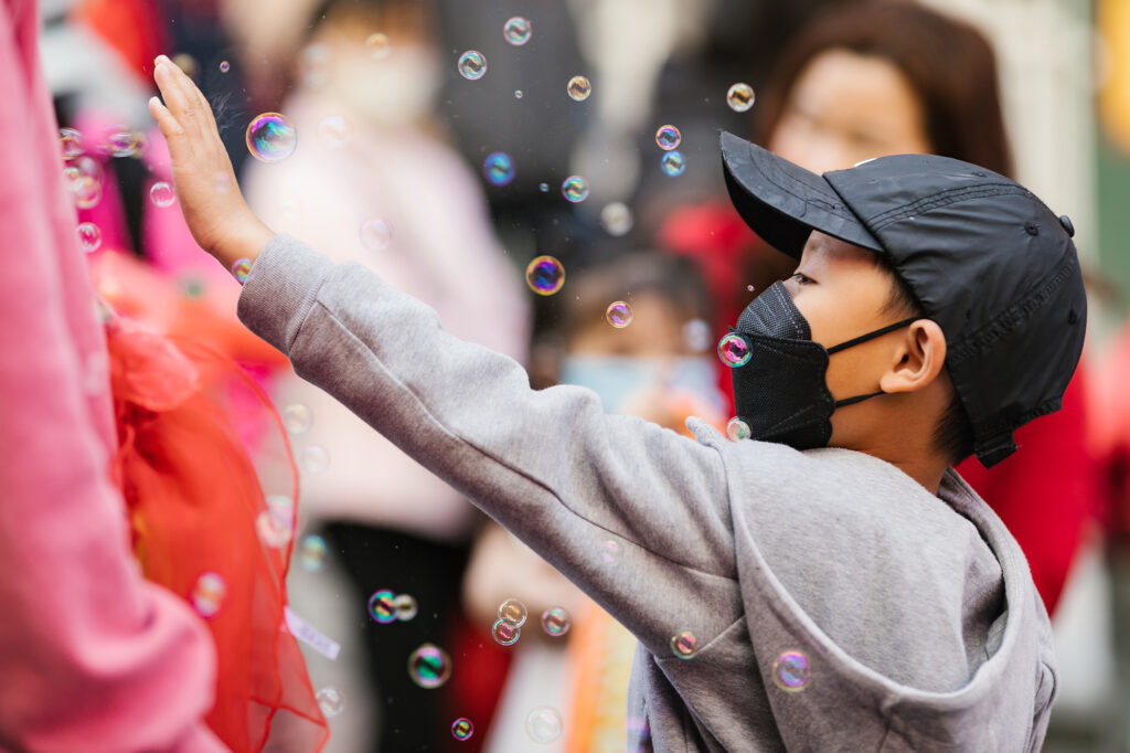 elementary aged boy reaching his arm up through bubbles blown on crowded street