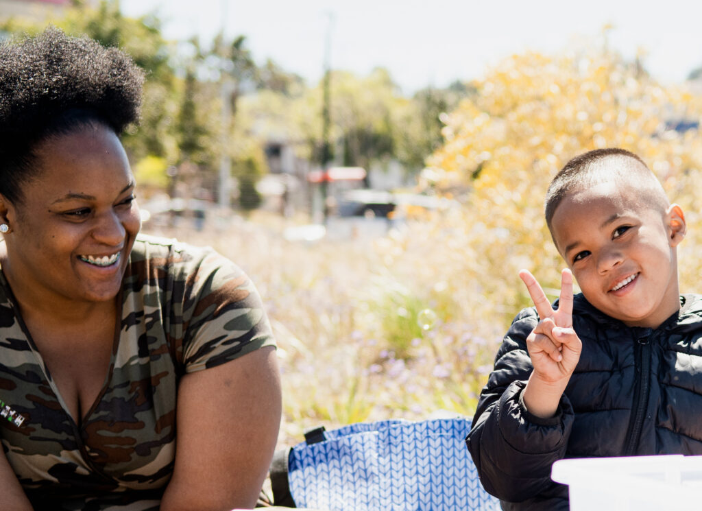 young boy outside on picnic blanket with mother, smiling at camera