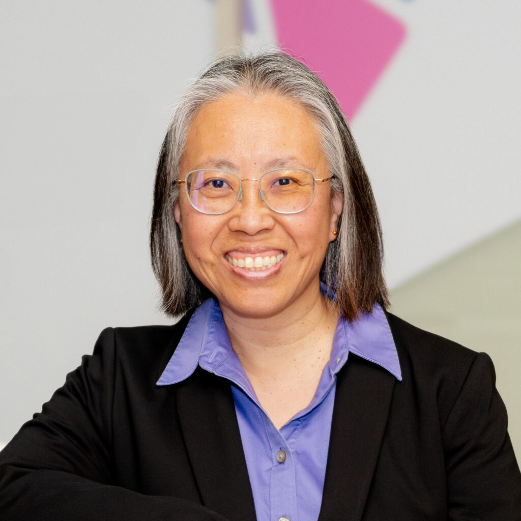 Headshot of a deputy director, wearing a black suit and purple collar shirt, smiling at the camera.