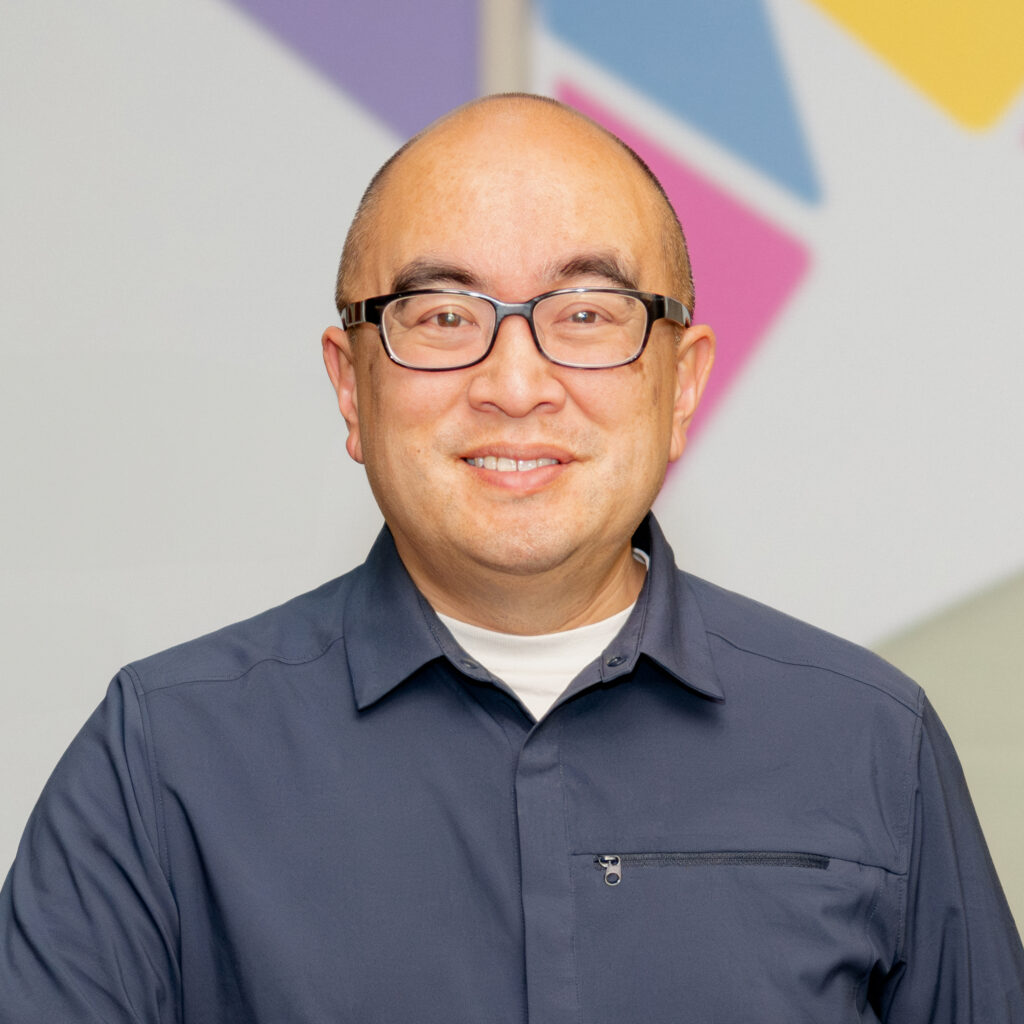 Headshot of a deputy director, wearing a dark grey collared shirt and smiling at the camera.