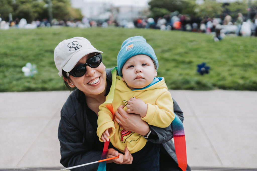 mother holding infant child outside, smiling at camera
