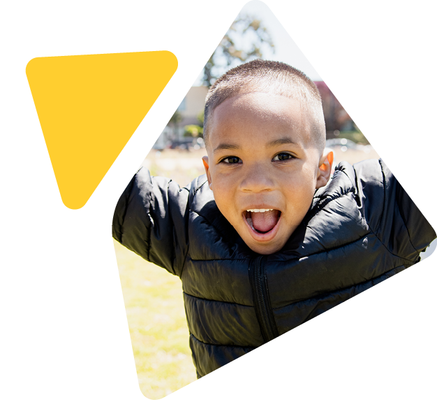 Young boy outside with arms lifted smiling at camera