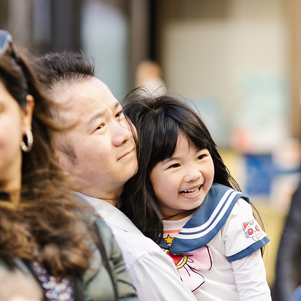 father holding smiling toddler daughter at street festival