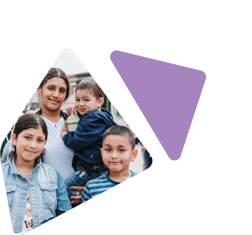 Mother holding toddler aged child with young son and daughter standing in front of her, facing camera