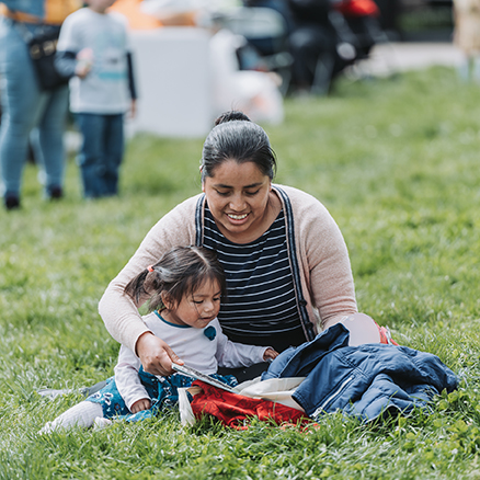 mom with daughter sitting on grass in a park reading