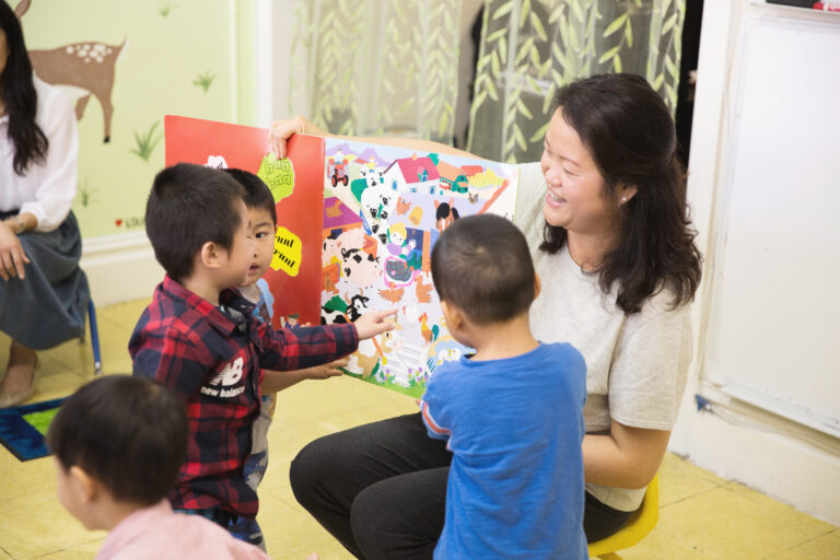 teacher reading large book to young children, sitting on floor